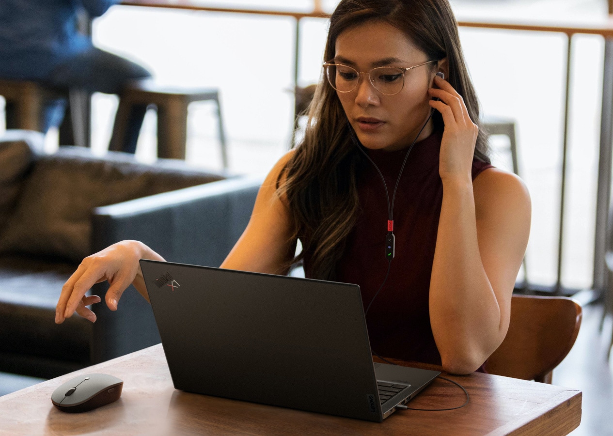 A girl wearing lenovo headphones listen to music while working on her Laptop